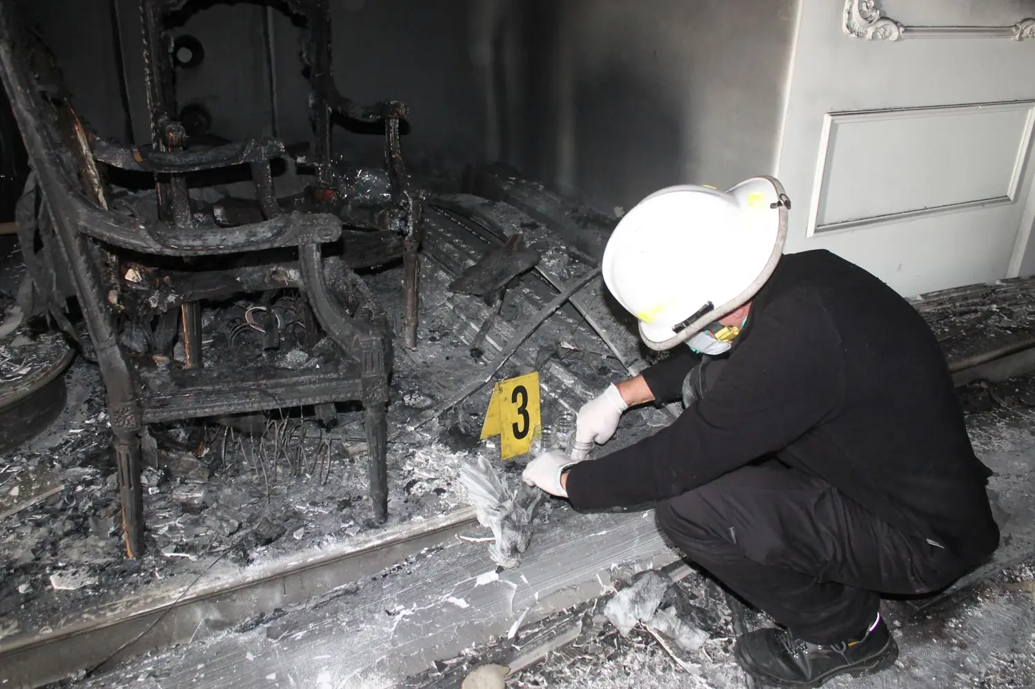 Un tecnico con il casco rileva un reperto tra i resti di un incendio