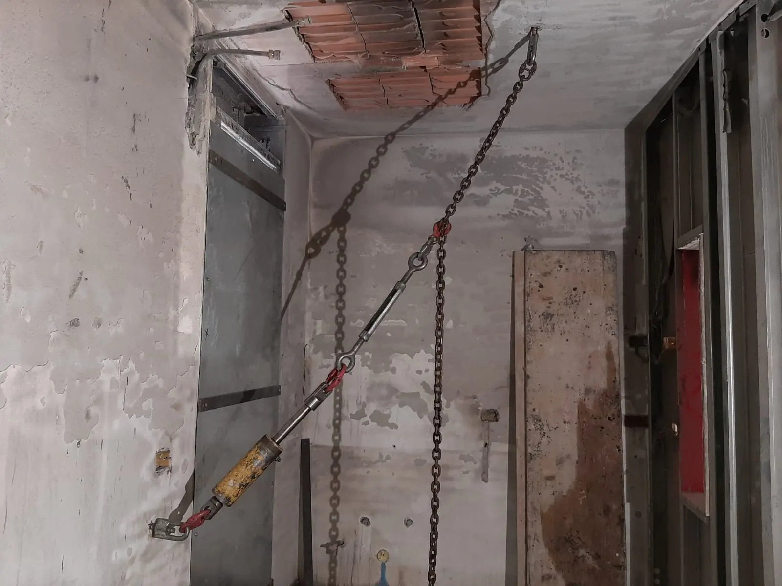 Un martinetto idraulico e delle catene ancorati al solaio e alla parete di un locale annerito da un incendio, durante una prova statica